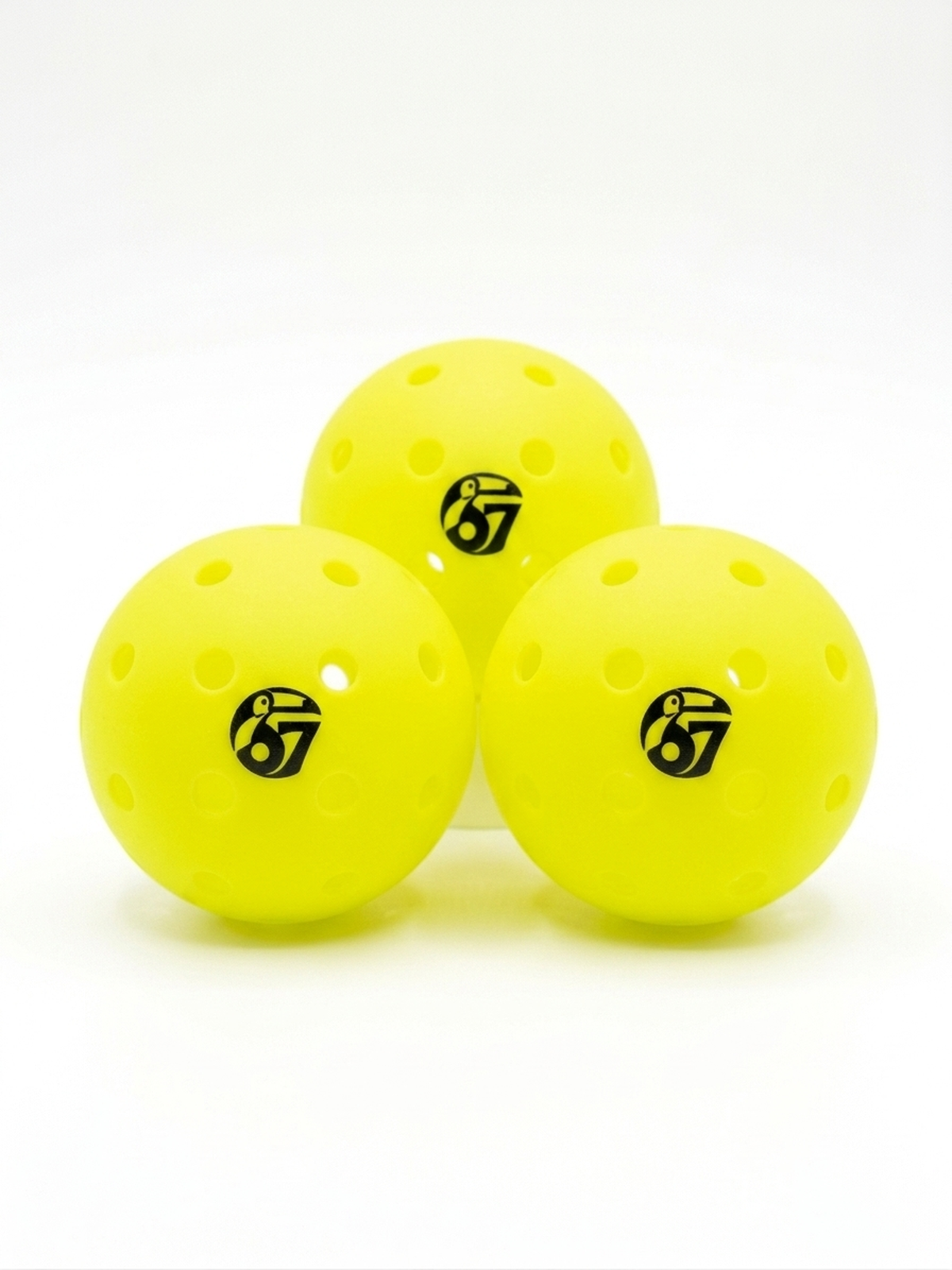 Three yellow perforated pickleballs with the number 67 logo on a white background