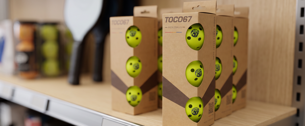 Box of TOCO67 branded yellow pickleballs on a retail shelf.